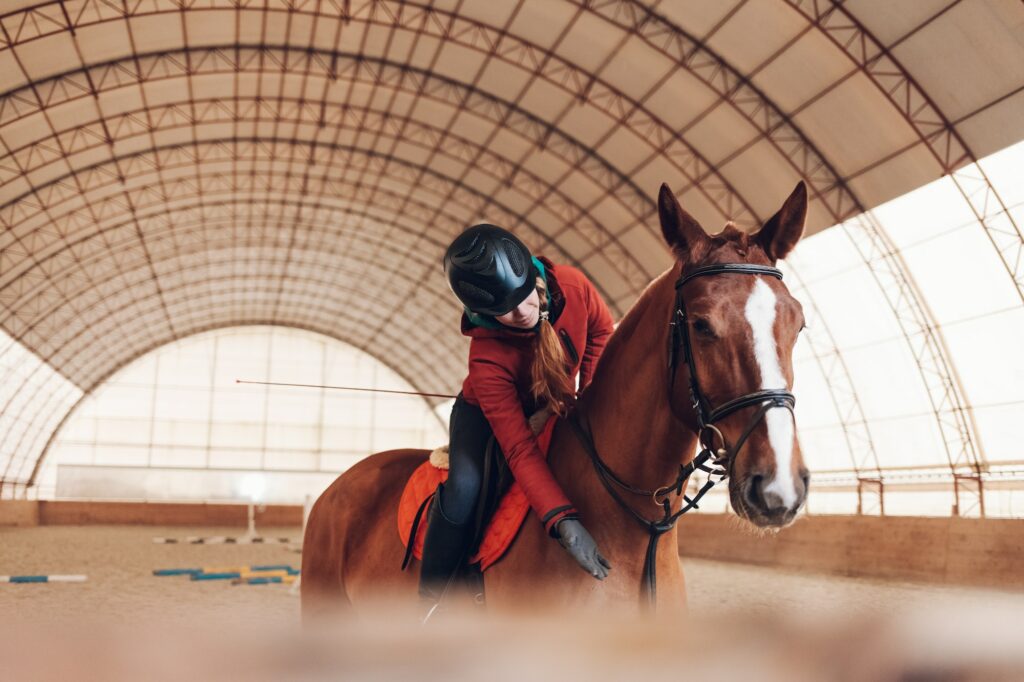 Reiterin mit Helm auf einem Pferd in einer Trainingshalle